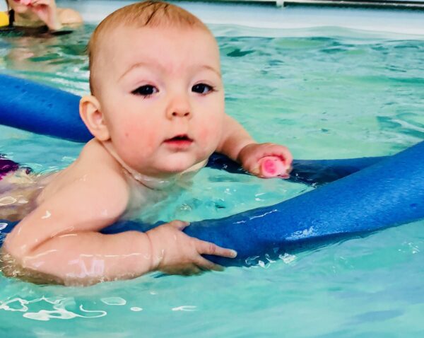 Baby swimming on noodle and catching toy